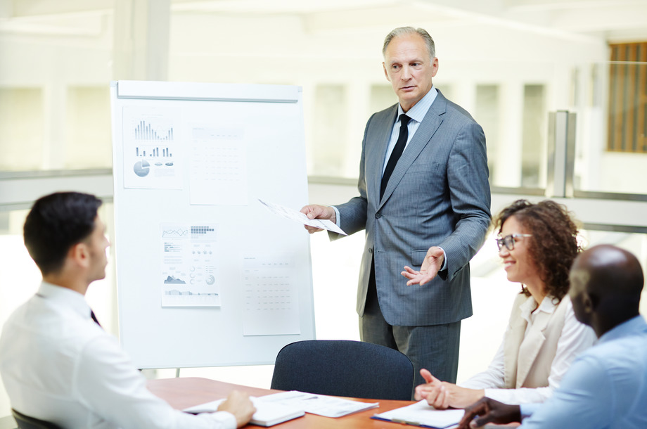 Confident senior business expert with paper standing by whiteboard